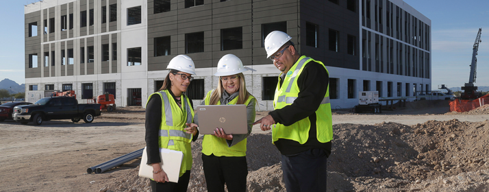 Three workers looking at laptop in front of new building